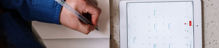 A person writing on a notebook while using an ipad