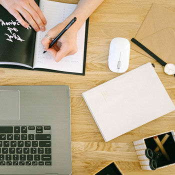 A woman using laptop and notes to study for NCLEX