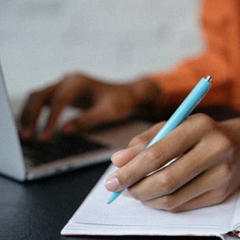 A woman doing a research on her laptop and taking notes