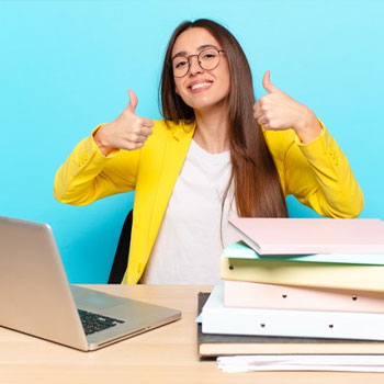 female student happy and giving a thumbs up with her laptop and books on desk