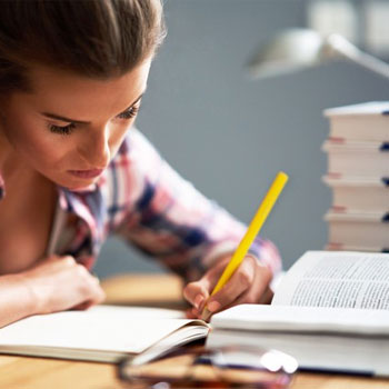 woman writing on a notebook with stack of books open