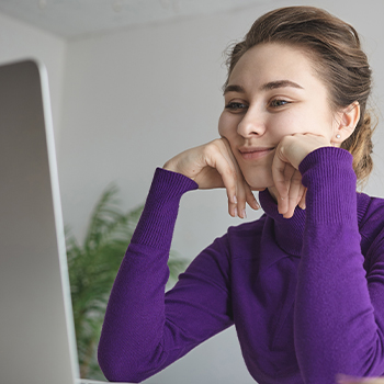 Woman in purple sweater smiling in front of the laptop