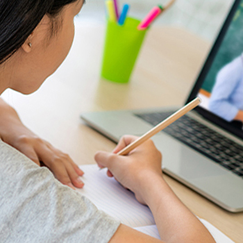 A student taking down notes in front of a laptop