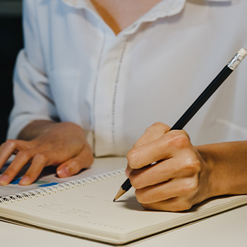 A man holding a pencil and writing some notes on his notebook