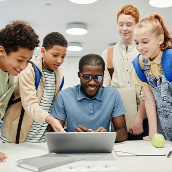 students and a male teacher looking at a laptop screen